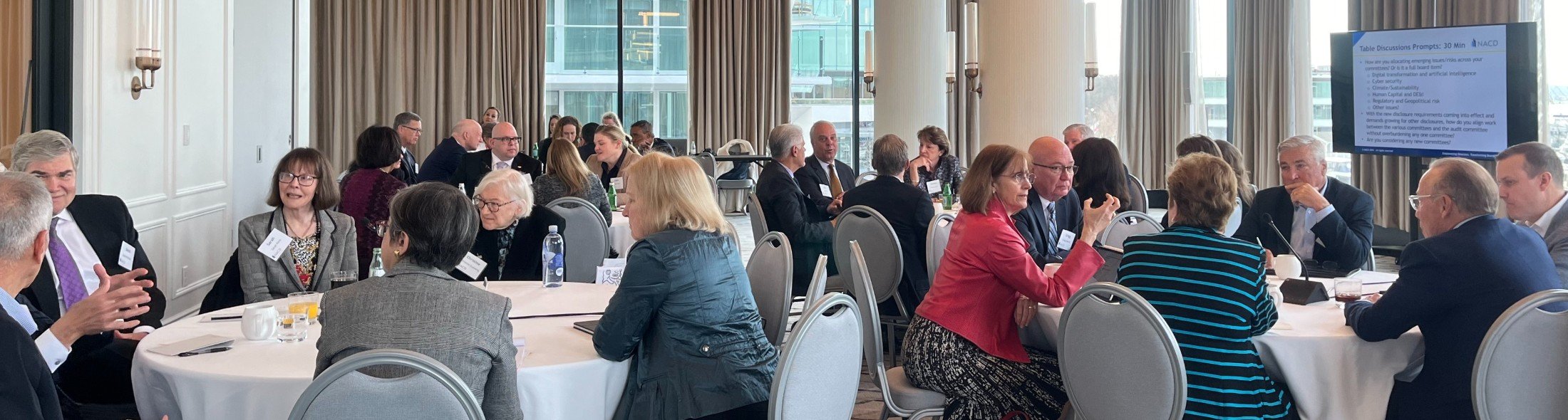 Directors seated at round tables engaging in discussions during a board leadership event